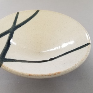 Puede incluir: Un cuenco de cerámica blanca con pinceladas negras en el borde. El cuenco es ligeramente curvo y tiene un acabado brillante.