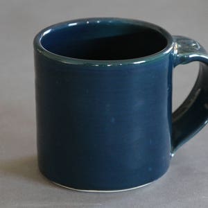 Peut inclure: Une tasse en céramique bleu turquoise foncé avec une anse arrondie. La tasse a une finition lisse et brillante.