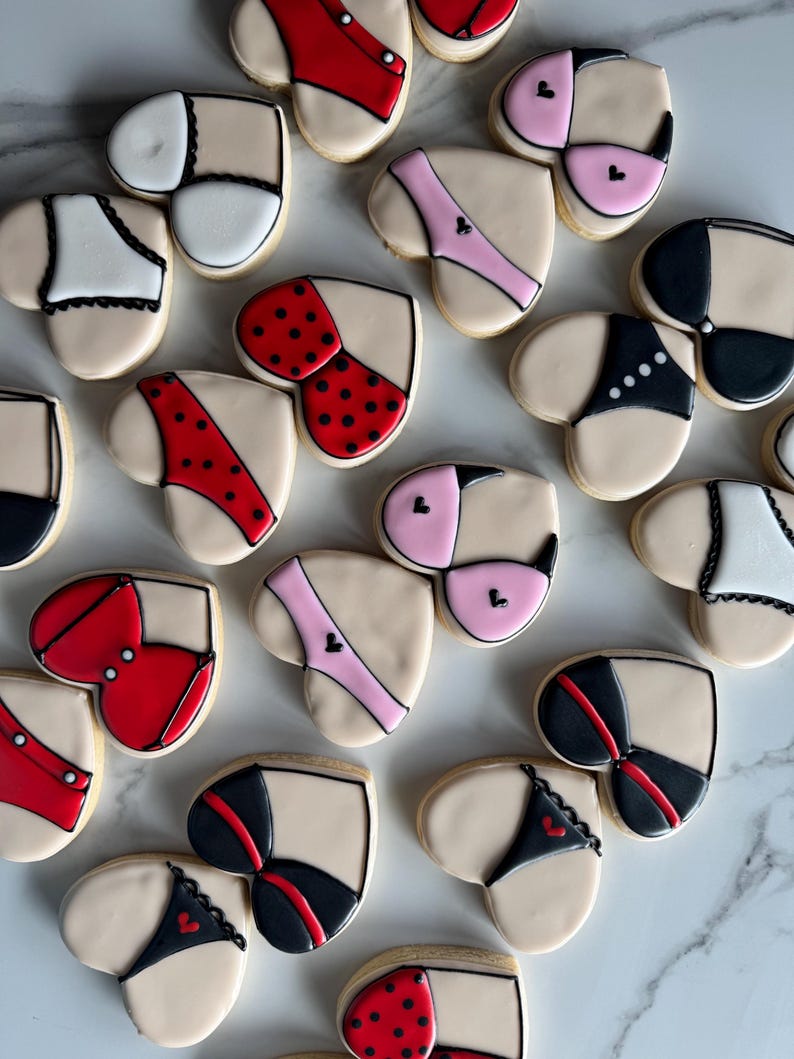 May include: Assortment of heart-shaped cookies decorated with various lingerie designs. The cookies feature different colors and patterns, including red, black, pink, white, and polka dots.