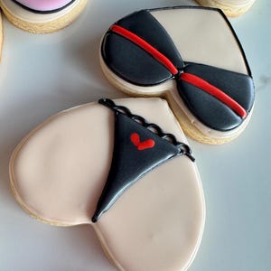 May include: Three heart-shaped sugar cookies decorated with black and red icing. The cookies are decorated with a bra and panty design.