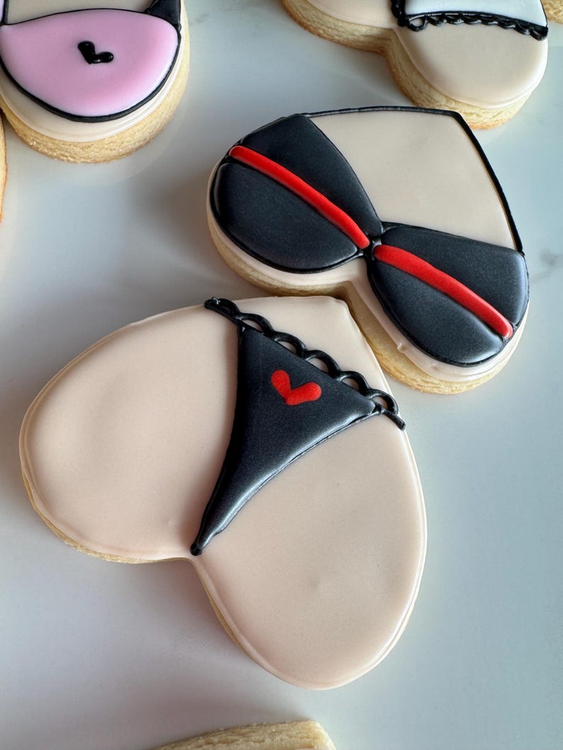May include: Three heart-shaped sugar cookies decorated with black and red icing. The cookies are decorated with a bra and panty design.