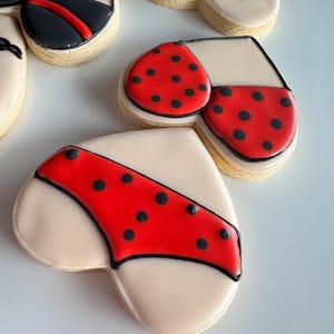 May include: Heart-shaped cookies decorated with red and black icing, resembling lingerie. The cookies have a white background and black outlines.