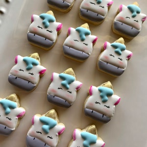 May include: A collection of twelve unicorn-shaped sugar cookies decorated with white, blue, and pink icing. The cookies are arranged in a circle on a white surface.