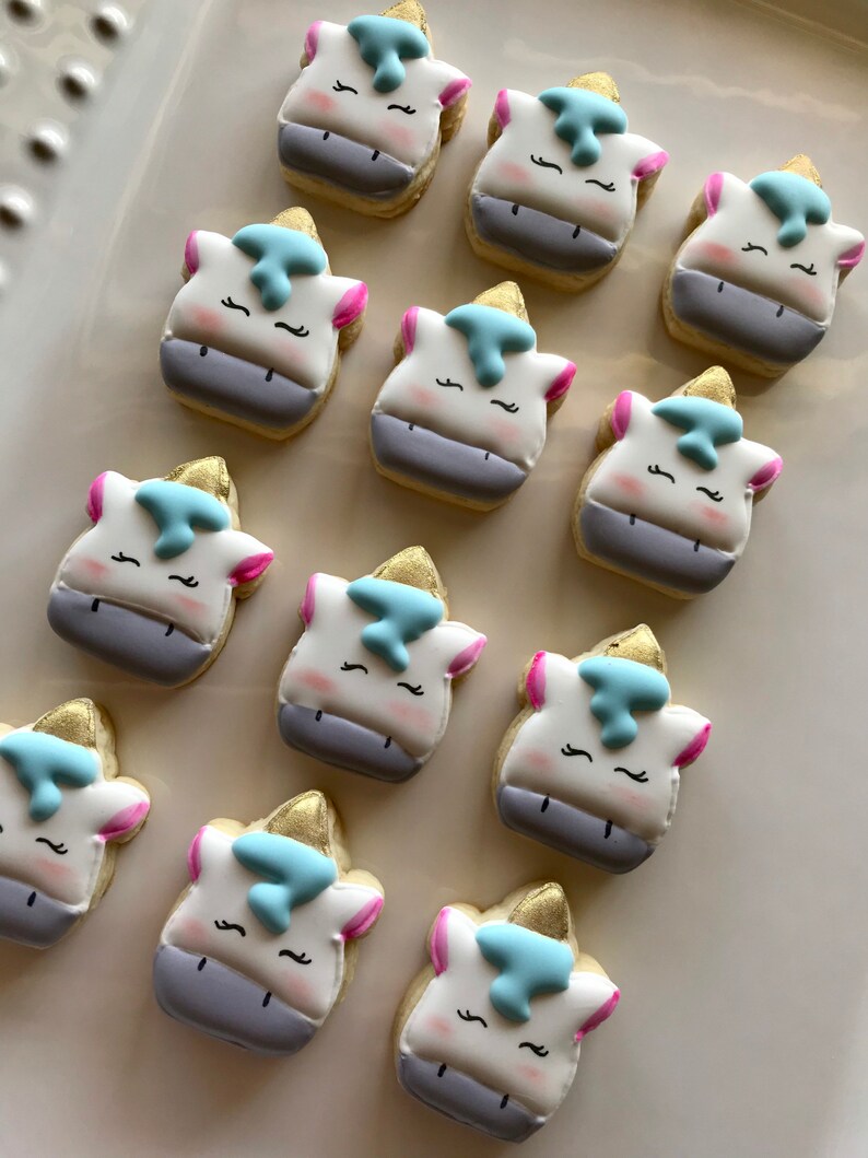 May include: A collection of twelve unicorn-shaped sugar cookies decorated with white, blue, and pink icing. The cookies are arranged in a circle on a white surface.