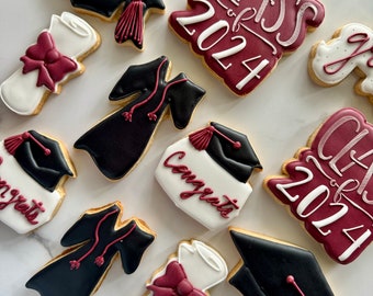 Può includere: Una collezione di biscotti a tema laurea decorati con glassa reale. Le forme includono tochi neri con nappe bordeaux, diplomi bianchi con fiocchi bordeaux, toghe nere e targhe bordeaux con la scritta Class of 2024.
