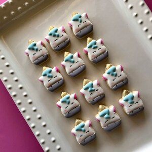 May include: A white platter with twelve unicorn-shaped sugar cookies decorated with blue, pink, and gold icing.