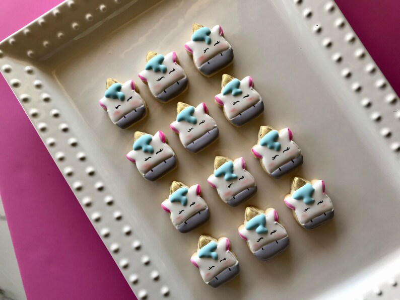May include: A white platter with twelve unicorn-shaped sugar cookies decorated with blue, pink, and gold icing.