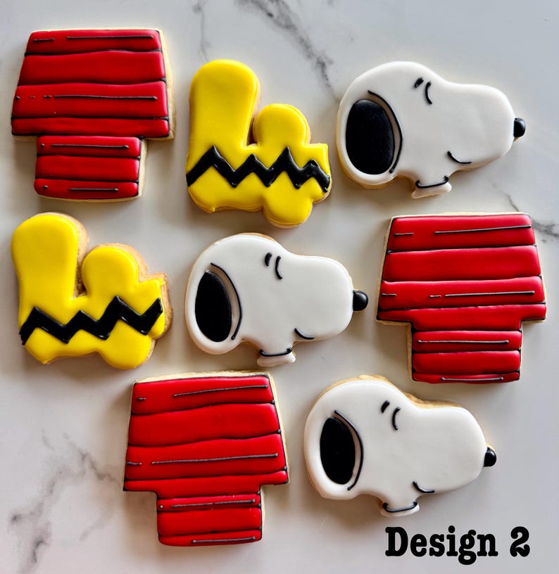 May include: A set of nine decorated sugar cookies featuring the characters Snoopy and Woodstock from the Peanuts comic strip. The cookies are decorated with red, yellow, black, and white icing. The cookies are arranged in a pattern on a white surface. Design 2.