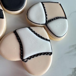May include: Two heart-shaped sugar cookies decorated with black icing and white icing. One cookie has a black bra design and the other has a black lace underwear design.
