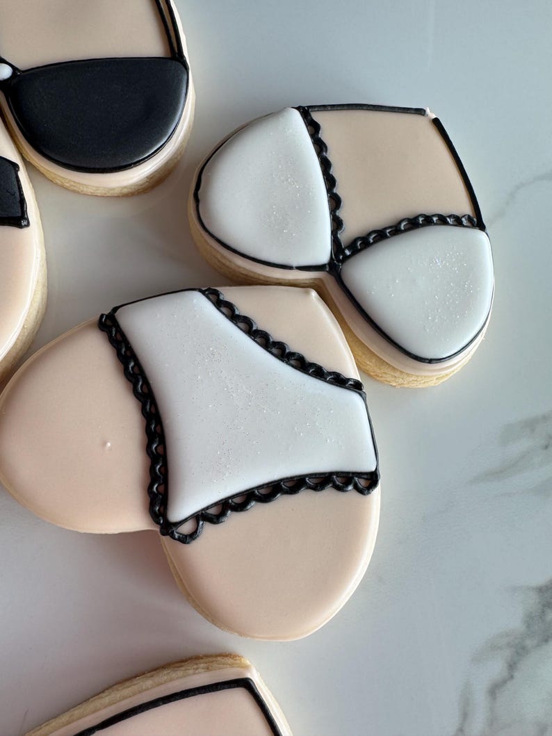 May include: Two heart-shaped sugar cookies decorated with black icing and white icing. One cookie has a black bra design and the other has a black lace underwear design.