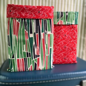 May include: Two fabric storage bags with folded-over tops. One bag features a red and white leaf pattern on the top and a green, red, black, and white geometric design on the body. The other bag has a red and white leaf pattern.