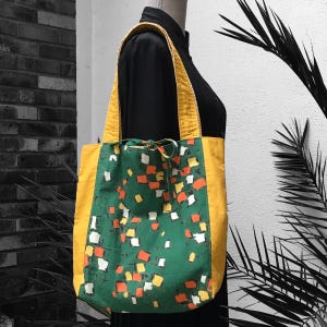 Wendbare, gefütterte Damen-Einkaufstasche aus Vintage-Stoff im Stil der 50er Jahre mit abstraktem Grafikdruck in Weiß, Gelb, Orange und schwarzen Kreisen auf grünem Hintergrund