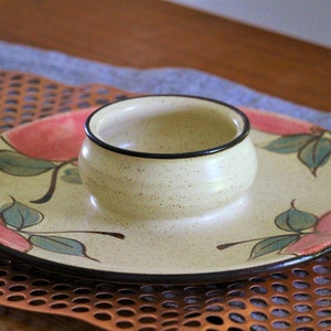 May include: A ceramic serving dish with a small bowl in the centre. The dish is decorated with a floral pattern in shades of pink, green, and brown. The bowl is white with a black rim.