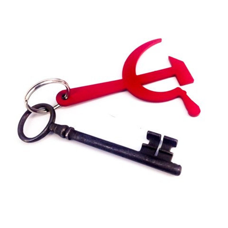 Pode incluir: Um chaveiro de metal vermelho em forma de martelo e foice preso a uma chave esqueleto antiga.