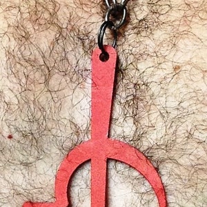 Pode incluir: Um pingente de metal vermelho em forma de martelo e foice, pendurado em uma corrente prateada.