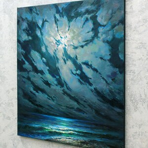 May include: A painting of a dark blue ocean scene with a bright white moon shining through dark blue clouds. The ocean is a deep blue with white waves and a light blue horizon.