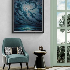 May include: A framed painting of a dark blue seascape with a bright moon shining through the clouds. The painting is hanging on a white wall above a teal blue armchair and a black side table.