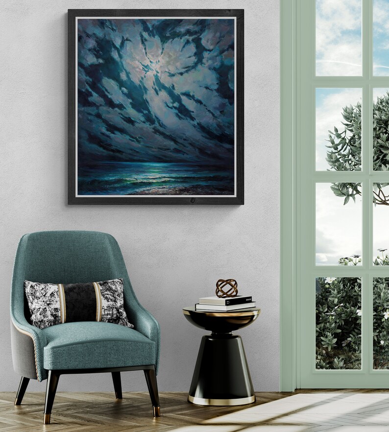 May include: A framed painting of a dark blue seascape with a bright moon shining through the clouds. The painting is hanging on a white wall above a teal blue armchair and a black side table.