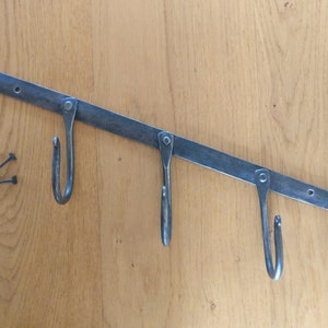 May include: A metal wall-mounted hook rack with three hooks. The rack is made of black metal and has a decorative scroll design at each end. The hooks are curved and are ideal for hanging kitchen utensils or other items.