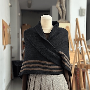May include: A black knitted shawl with brown stripes, draped over a mannequin wearing a plaid skirt.
