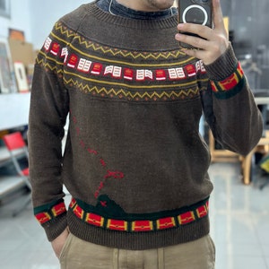 May include: A brown knitted sweater with a colorful geometric pattern around the neck and cuffs. The sweater has a red, green, and yellow design on the front.