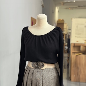 May include: A black sweater with a scoop neck and long sleeves. The sweater is worn over a plaid skirt with a decorative belt.