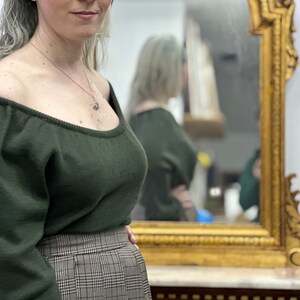 May include: A woman wearing a dark green off-the-shoulder sweater with long sleeves and a plaid skirt.