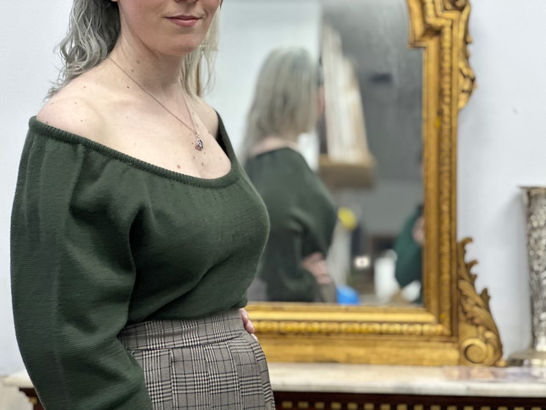May include: A woman wearing a dark green off-the-shoulder sweater with long sleeves and a plaid skirt.