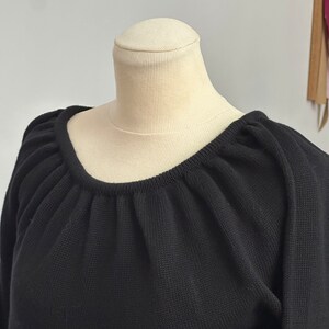 May include: Black knitted sweater with a gathered neckline and long sleeves.
