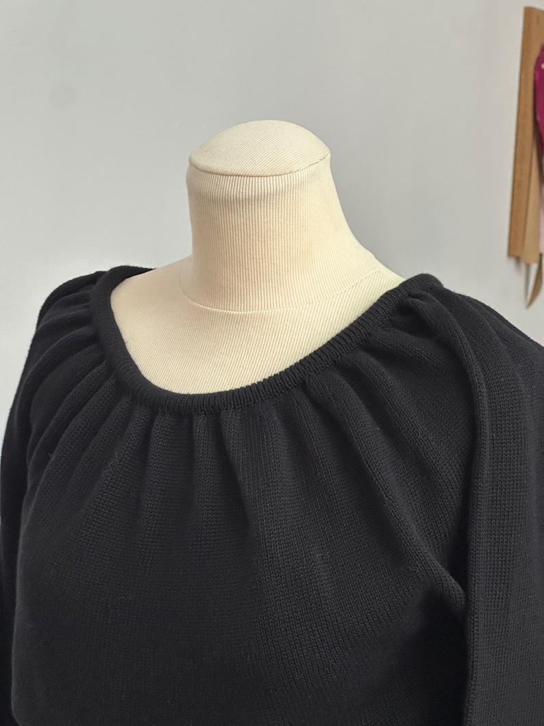 May include: Black knitted sweater with a gathered neckline and long sleeves.