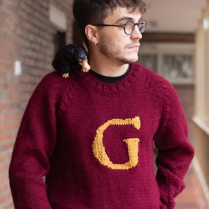 Man wearing a burgundy Magical Christmas Weasley sweater handwoven and personalized with a custom capital letter G on his chest