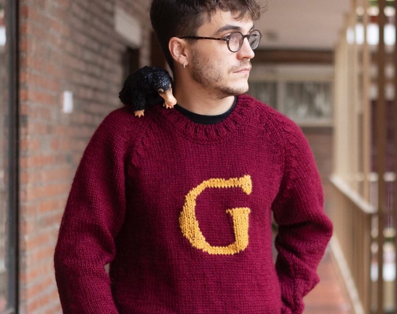 Man wearing a burgundy Magical Christmas Weasley sweater handwoven and personalized with a custom capital letter G on his chest
