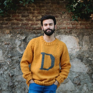 Boy wearing a mustard Magical Christmas Weasley sweater handwoven and personalized with a custom capital letter D on his chest