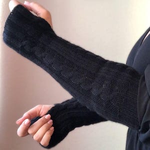 May include: Black knitted arm warmers with a cable knit pattern.