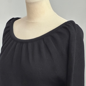 May include: Black knitted sweater with a wide, off-the-shoulder neckline. The sweater has a relaxed fit and a slightly gathered neckline.