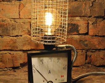 Könnte beinhalten: Eine Lampe im Vintage-Stil, hergestellt aus einem wiederverwendeten Elektrizitätszähler und einer Leuchte mit Drahtkäfig. Das Zifferblatt des Zählers hat eine Nadel, die auf den Buchstaben "A" zeigt, und Zahlen von 0 bis 100.