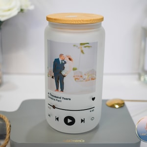 May include: A white frosted glass jar with a bamboo lid, featuring a photo of a couple on their wedding day. The jar has a music player design with the song title "A Thousand Years" by Christina Perri and a play button.