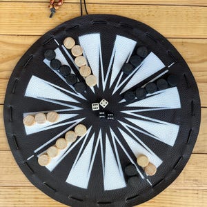 May include: A black leather game board with white markings and a circular design. The board has wooden playing pieces in black and natural wood colors. Two white dice are in the center of the board.