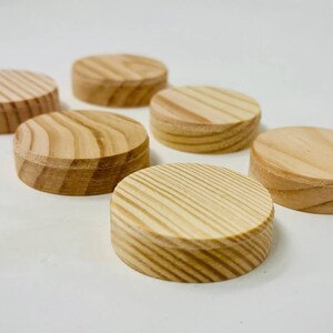 Könnte beinhalten: Sechs kleine, runde Holzobjekte. Sie sind hellbraun mit sichtbarer Holzmaserung und natürlicher Oberfläche. Die Oberseiten sind kreisförmig, die Seiten gerade. Die Objekte liegen auf einer weißen Oberfläche. Jeder Gegenstand hat etwa 3 cm Durchmesser.
