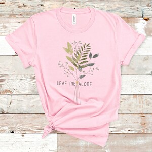 May include: Pink t-shirt with a green and gray floral design and the text "Leaf Me Alone."