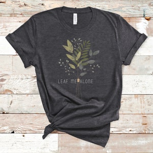 May include: A dark gray t-shirt with a green and brown floral design and the text "LEAF ME ALONE" printed on the front.