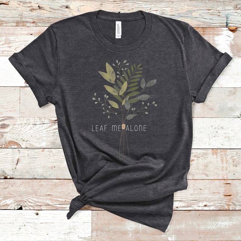 May include: A dark gray t-shirt with a green and brown floral design and the text "LEAF ME ALONE" printed on the front.
