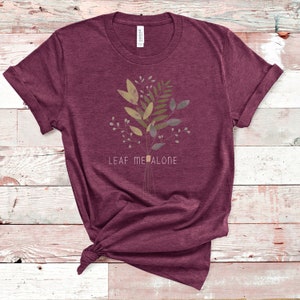 May include: A maroon t-shirt with a floral design and the text "LEAF ME ALONE" printed on the front.