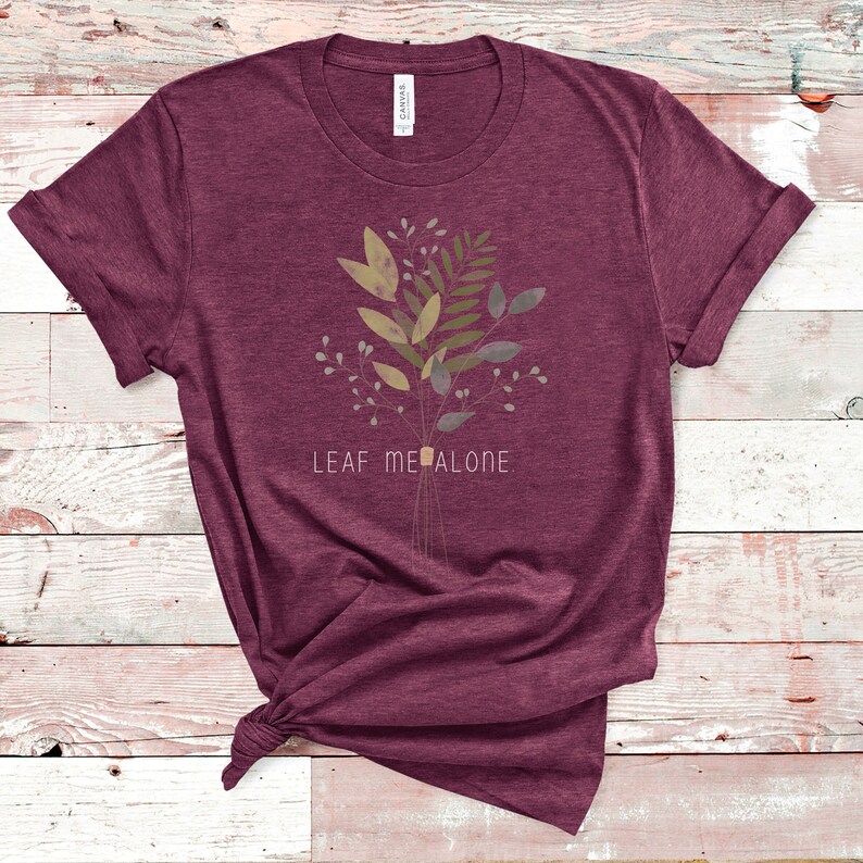 May include: A maroon t-shirt with a floral design and the text "LEAF ME ALONE" printed on the front.