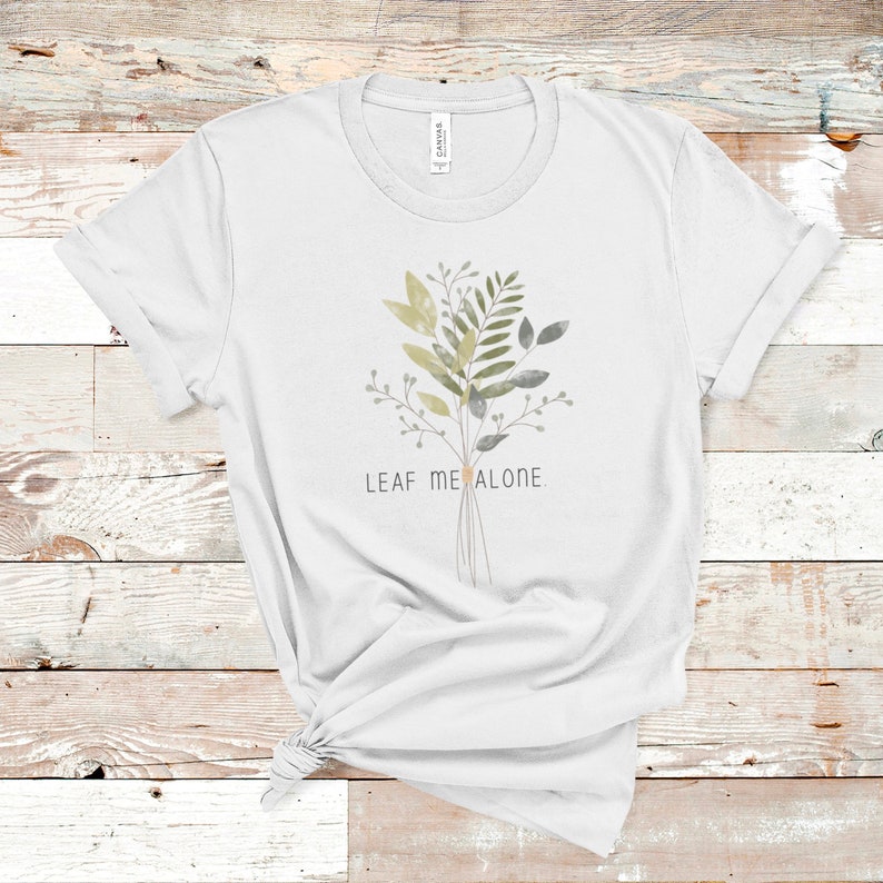 May include: White t-shirt with a watercolor illustration of a bouquet of leaves and the text "LEAF ME ALONE".
