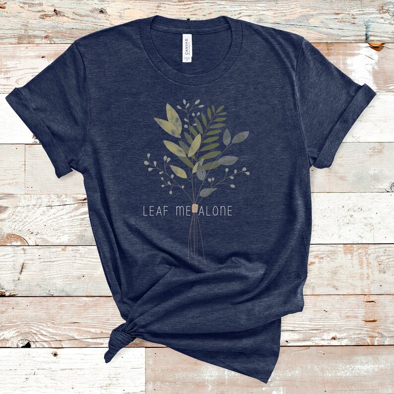 May include: A navy blue t-shirt with a watercolor-style illustration of a bouquet of green leaves and the text "LEAF ME ALONE".