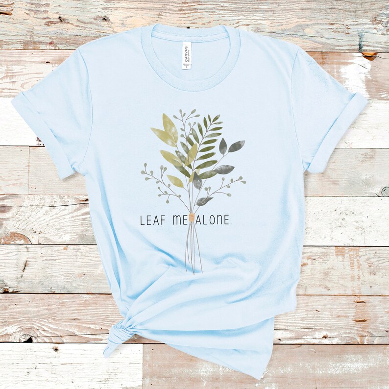 May include: Light blue t-shirt with a watercolor-style illustration of a bouquet of green leaves and the text "LEAF ME ALONE."