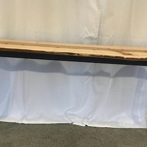 May include: A long, rectangular console table with a natural wood top and black metal legs. The tabletop is light-colored with a live edge, and the legs are a simple, geometric design. The table is approximately 60 inches long.