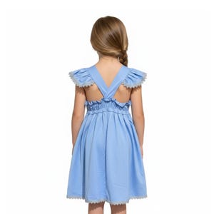 May include: A light blue dress with a V-back design. The dress features ruffled shoulder straps and a gathered waist. The edges of the dress are trimmed with a delicate white lace. The dress is designed for children.