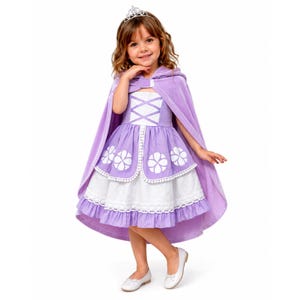 May include: A lavender dress featuring a white bodice with crisscross detailing, a skirt with white floral patterns and a ruffled hem, and a matching lavender hooded cape. The outfit is accessorized with a silver-toned tiara and white ballet flats.